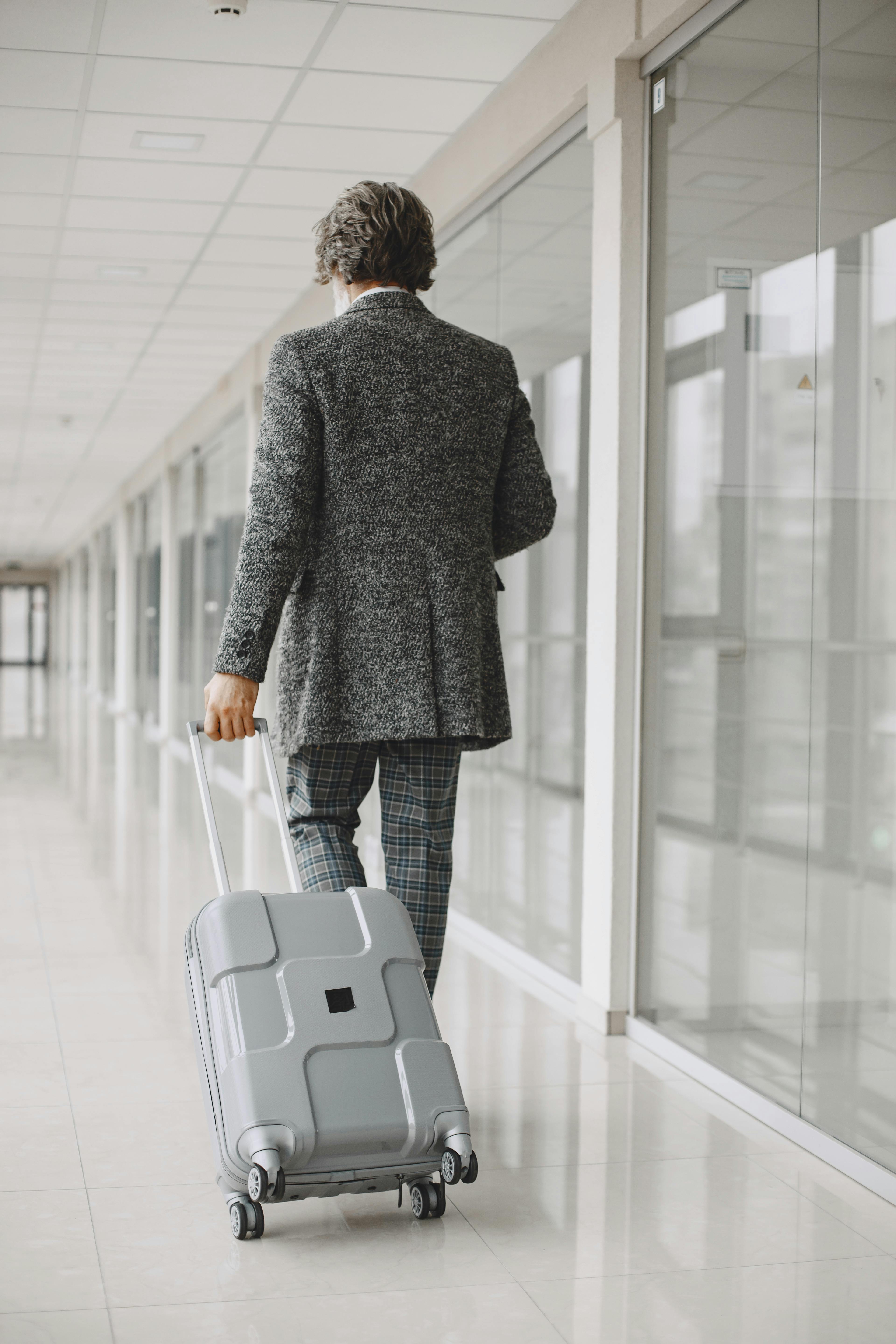 Business professional in gray suit walking with luggage at airport terminal - LuxRide executive airport transfer service