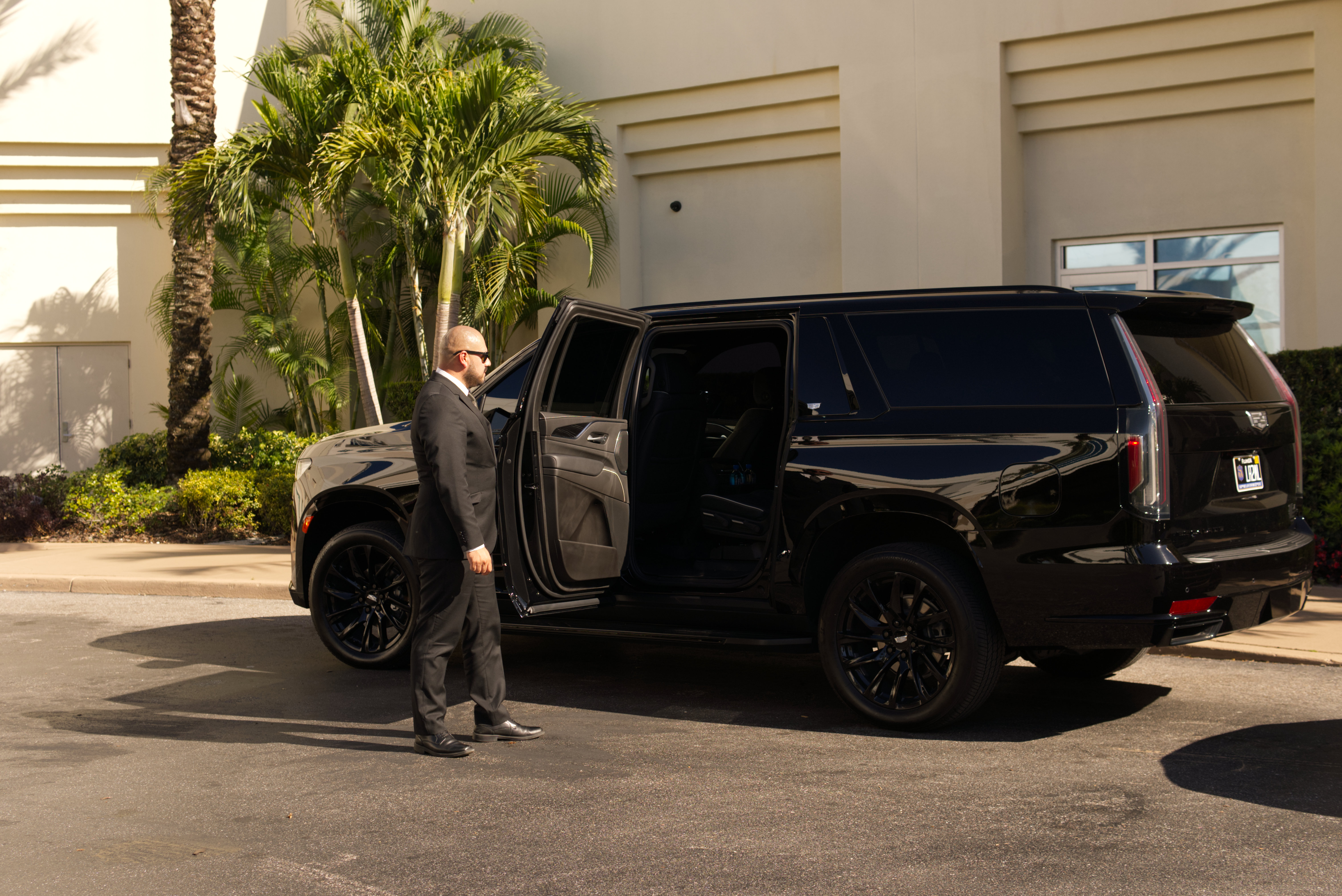 LuxRide professional chauffeur holding open door of black Cadillac Escalade in Tampa Bay Florida
