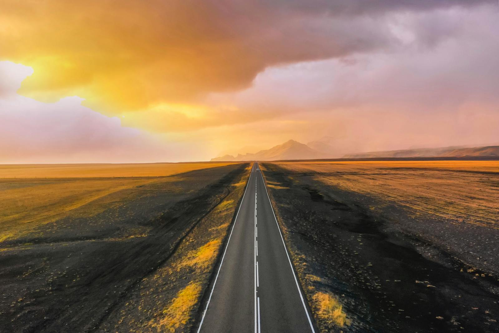 Long open highway stretching to horizon under dramatic golden sunset sky - long-distance travel